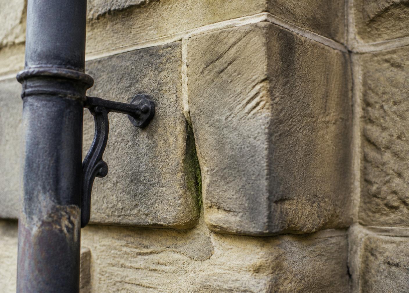 Detail einer verwitterten fränkischen Sandsteinfassade mit gusseiserner Fallrohrschelle